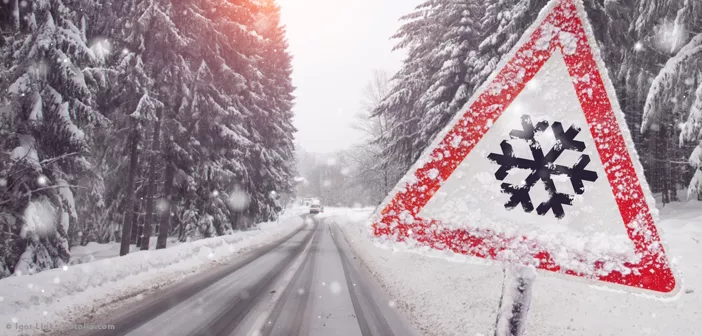 Verschneite Straße mit rotem dreieckigem Warnschild mit einer Schneeflocke